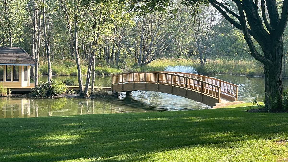 Custom wood footbridge with railing crossing a backyard pond in Chelsea, MI